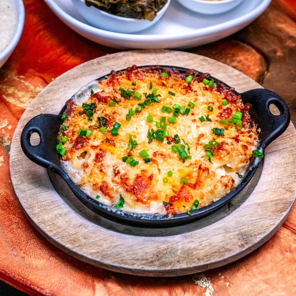 A cast iron skillet of baked macaroni and cheese, topped with green onions, on a wooden board.