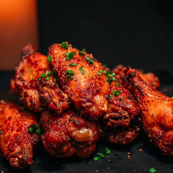 Close-up of crispy, seasoned chicken wings garnished with green onions on a dark surface.