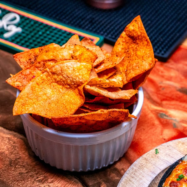 A white bowl filled with crispy, seasoned tortilla chips on a wooden table.