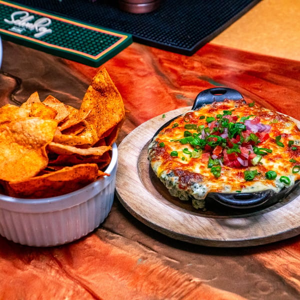 Cheesy dip with pico de gallo and green onions in a skillet, served with tortilla chips.